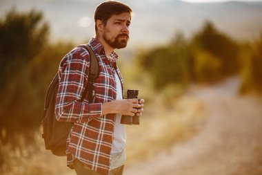 Tepedeki dürbüne bakan adam. Sırt çantalı bir adam. Vadi manzarasında yürüyüş yapan genç beyaz bir adam.