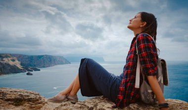 Yazın deniz kıyısında sırt çantalı bir turistle seyahat eden bir kadın. Kudretli Kayalıklar Arasında Güzel Bulutların Tadını Çıkarıyorum Okyanusla Buluşma. özgürlük fikri ve konsepti, tatil ve keşif