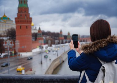 Genç Asyalı güzel turist Moskova Kremlin, Rusya 'nın arka planında cep telefonuyla fotoğraf çekiyor.