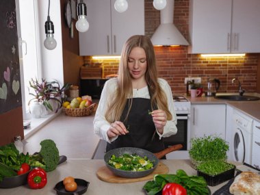 A young blonde happy lady standing in the kitchen while cooking healthy food. Healthy Lifestyle Concept. Cooking at home. decorating and serving the finished dish
