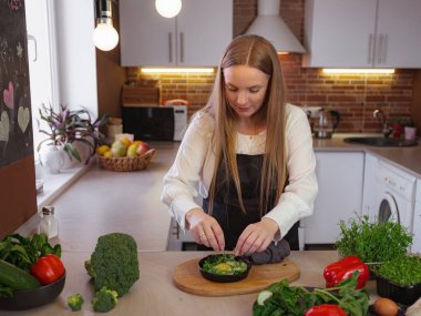 A young blonde happy lady standing in the kitchen while cooking healthy food. Healthy Lifestyle Concept. Cooking at home. decorating and serving the finished dish