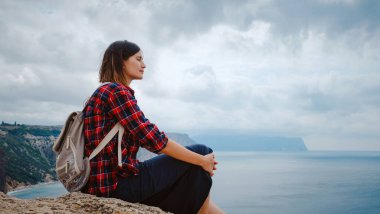 Yazın deniz kıyısında sırt çantalı bir turistle seyahat eden bir kadın. Kudretli Kayalıklar Arasında Güzel Bulutların Tadını Çıkarıyorum Okyanusla Buluşma. özgürlük fikri ve konsepti, tatil ve keşif