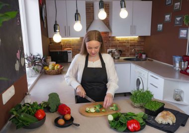 Sağlıklı yemek pişirirken mutfakta duran mutlu, genç bir sarışın bayan. Sağlıklı Yaşam Tarzı Konsepti. Evde yemek pişirmek. Yemek yapmak için sebze doğrama