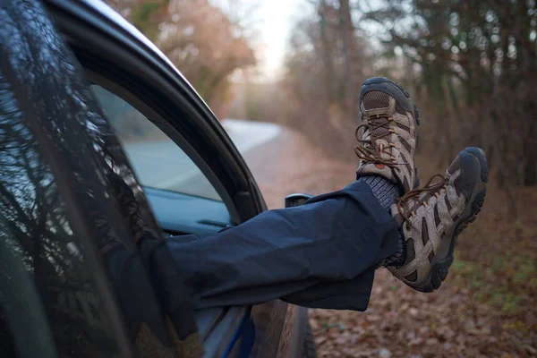 male feet in trekking boots sticking out the car window. Autumn car ride at sunset in the woods. The concept of freedom of movement. Driving through a weekend