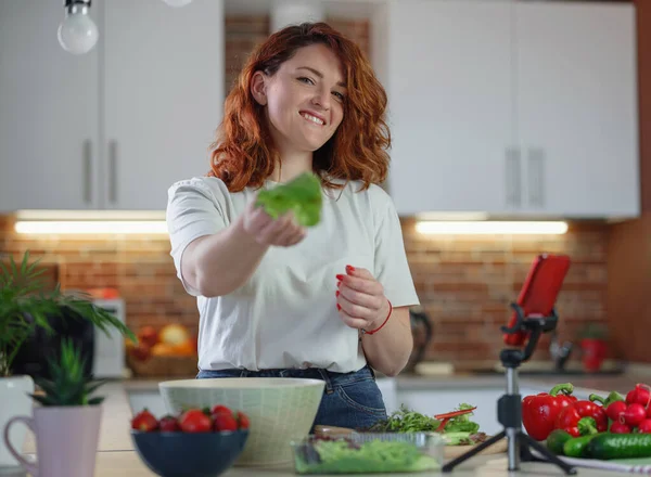 Young pretty woman blogger shoots a video of a salad recipe on a smartphone camera. The concept of healthy eating. Food blog concept