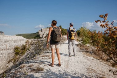 İki adam kayalık yamaçlarda yürüyüş çubuklarını kullanarak sırt çantalarını taşıyorlar. Dağlar Vadisi, insanların yanı sıra manzaralı. Doğaya yaz yolculuğu