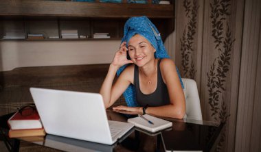 Kafasında mavi havlu olan kadın evden uzakta ofis işi yapıyor. Bilgisayar kullanarak. Çevrimiçi eğitim ve çalışma mesafesi. Serbest Çalışan