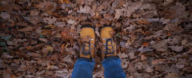 Sonbahar yaprakları üzerinde sarı çizme giymiş kadın bacaklarının kavramsal görüntüsü. Doğada yürüyen ayaklar