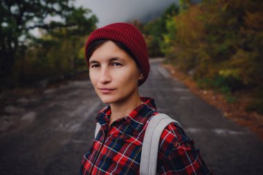 Yol ve orman arka planında mutlu Asyalı kız çantası tatil gezisi konseptinde dinlenme zamanı, klasik ton rengi ve yumuşak odak noktası