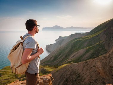 Genç adam dağların arka planında tek başına seyahat eder. Açık havada seyahat etmenin yaşam tarzı. Önündeki mavi denizle mesafeye bakıyorum..