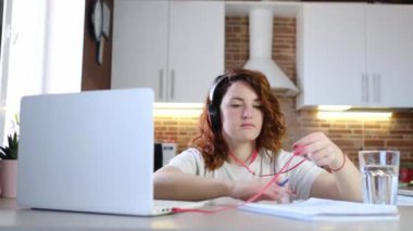 COVID-19 salgınında kendini izole etme. Ev ofisinden çalış ve çalış. Kızıl saçlı genç bir kadın bir webinar ya da öğretmeni dinlerken not alır..