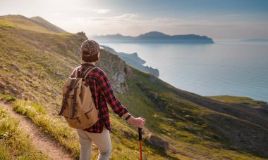 Toprak yolda yürüyen kadın yürüyüşçü. Yürüyüş sırasında sırık kullanan bir kadın. Güneşli deniz manzarasının tadını çıkarıyor. Dağ ve kıyı seyahati, özgürlük ve aktif bir yaşam tarzı