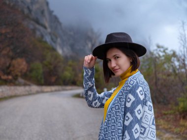 Şapkalı ve pançolu şık hippi kadın dağ yolunda yürüyor. Seyahat ve seyahat tutkusu kavramı. İnanılmaz bir atmosferik an.