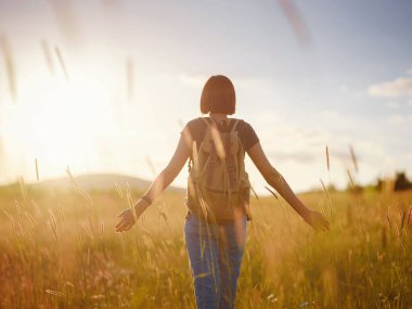 Günbatımında bir tarlada sırt çantalı şık genç bir kadın. Özgürlük ve doğa kavramı. Yumuşak odak
