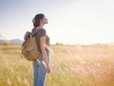 Günbatımında bir tarlada sırt çantalı şık genç bir kadın. Özgürlük ve doğa kavramı. Yumuşak odak