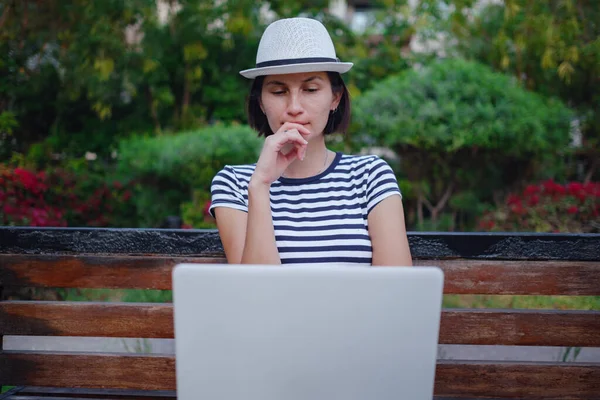 woman looking for a job with a laptop in a city park in the summer, Education online. Happy woman calling on laptop, talk by webcam, video conference.