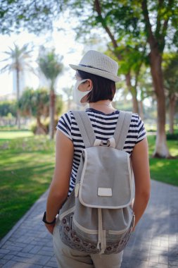 Yaz güneşli bir hayat tarzı var. Genç stil sahibi Asya 'lı bir kadın sokakta yürüyor. Yüzüne şık kıyafetler ve koruyucu bir maske takıyor.