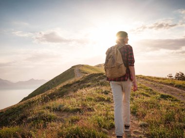 Sırt çantalı genç bir Asyalı kadın yazın gün batımında dağa tırmanıyor. Dağ ve kıyı seyahati, özgürlük ve aktif bir yaşam tarzı