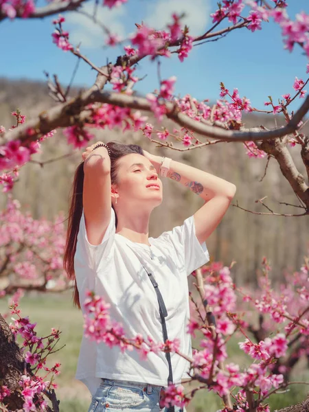 Piękna Kobieta Ciemnymi Włosami Białej Koszulce Wśród Kwitnących Drzew Brzoskwiniowych — Zdjęcie stockowe