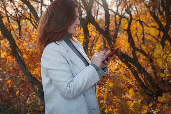 Positive female model in elegant coat enjoying autumn day. Outdoor photo of gorgeous curly woman talking on phone.