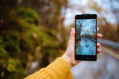 Ormanda sonbaharın muhteşem renklerini yakalamak için cep telefonu tutan bir kadın. Düş Kaçış