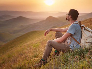 Sırt çantalı bir gezgin bir dağın tepesinde oturur ve kıyı manzarasının tadını çıkarır. Dağ ve kıyı seyahati, özgürlük ve aktif bir yaşam tarzı