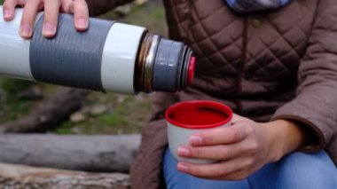 Bir kadın termostan sıcak, lezzetli çay doldurur..