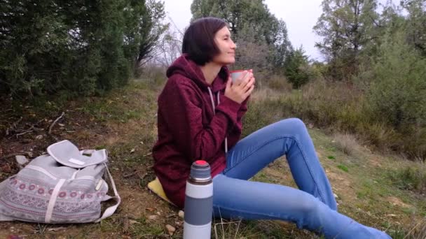 Wanita muda cantik dengan minuman panas menghabiskan liburan di antara hutan musim gugur. — Stok Video