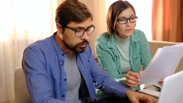 Серйозна молода пара, що тримає документи, платить внутрішні рахунки онлайн на ноутбуці — стокове відео