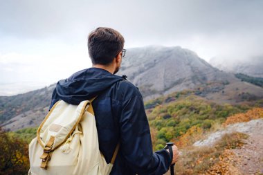 Sırt çantalı ve sopalı bir adam dağlarda yürüyüş yapıyor..