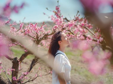 Parkta çiçek açan şeftali ağaçlarında siyah saçlı güzel bir kadın.