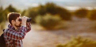 Tepedeki dürbüne bakan adam. Sırt çantalı bir adam..