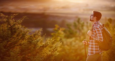 Sırt çantalı genç gezgin arka planda kayalık dağlarla dışarıda dinleniyor.