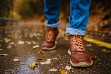 Sonbahar ormanlarında asfalt yolda yürüyen bir kadının ayakları.