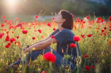 Güzel bir kadın gün batımında gelincik tarlasında meditasyon yapar.