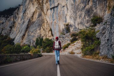Sonbahar sisli bir günde dağ yolunda tek başına yürüyen Asyalı hippi kadın.
