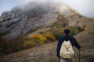 Sırt çantalı ve sopalı bir adam dağlarda yürüyüş yapıyor..