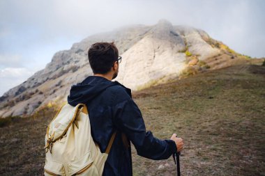 Sırt çantalı ve sopalı bir adam dağlarda yürüyüş yapıyor..