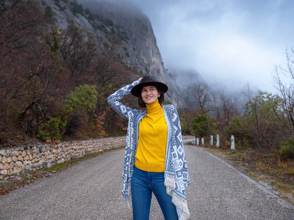 Elegante donna hipster in un cappello che cammina lungo una strada di montagna — Foto Stock