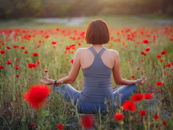 Een mooie vrouw mediteert op een papaverveld bij zonsondergang — Stockfoto