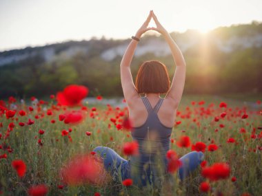 Güzel bir kadın gün batımında gelincik tarlasında meditasyon yapar.