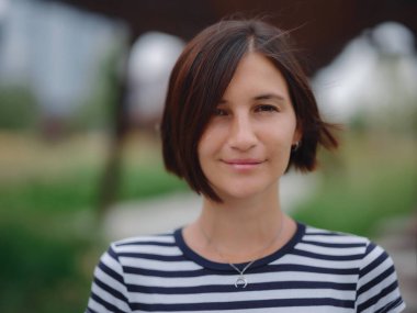 Güzel genç Asyalı kadın yaz günü çağdaş şehir parkında vakit geçiriyor. Kameraya bak.