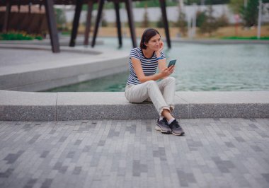 Genç bayan hipster arkadaşlarıyla internette cep telefonuyla sohbet ediyor ve müzik dinliyor. Güzel bir kadın parkta dinlenirken cep telefonundan mesaj okuyor.