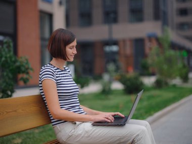 Dizüstü bilgisayarda çalışan genç Asyalı kız öğrenci şehir caddesindeki bankta oturuyor. Mutlu bayan mesafe öğrenimi, eğitim ve online alışveriş.