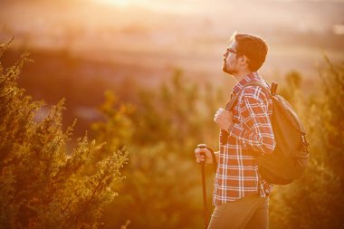 Sırt çantalı genç gezgin arka planda kayalık dağlarla dışarıda dinleniyor.