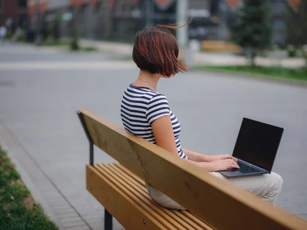 Estudiante trabajando en el ordenador portátil sentarse en el banco en la calle urbana de la ciudad. — Foto de Stock