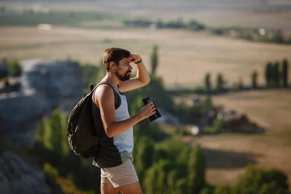 Kerl mit Ferngläsern in der Hand. Mann im T-Shirt mit Rucksack. — Stockfoto