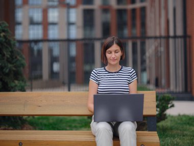 Dizüstü bilgisayarda çalışan genç Asyalı kız öğrenci şehir caddesindeki bankta oturuyor. Mutlu bayan mesafe öğrenimi, eğitim ve online alışveriş.