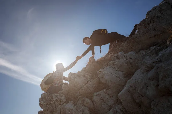 Silhouettes of two people climbing mountains and helping against the blue sky.