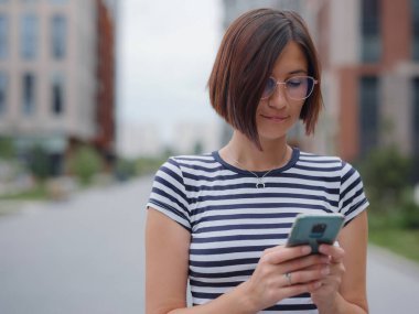 Sokakta cep telefonu kullanan gülümseyen kadın.